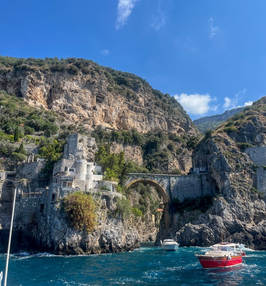 Boats below the cliffs and stone bridge of the Amalfi coast