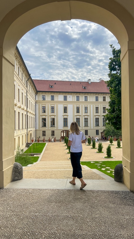 Megan walking through a stone archway into a palace courtyard
